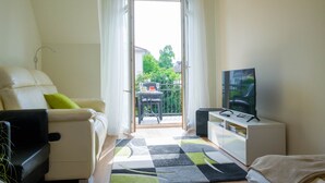 Ein modernes Wohnzimmer mit einer Couch, einem Fernseher und einem Balkon mit Tisch und Stühlen.