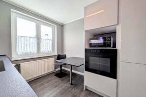 Kompakti keittiö, jossa on sisäänrakennettu uuni, ruokapöytä ja ikkuna, jossa on ohuet verhot.