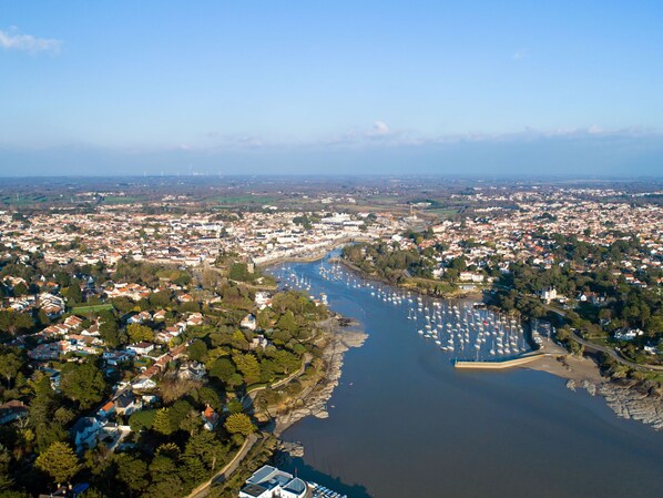 An aerial view of a coastal town with a marina filled with boats, surrounded by residential areas and greenery.
