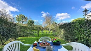 Taula a l'aire lliure amb vista a un jardí i un edifici al fons.