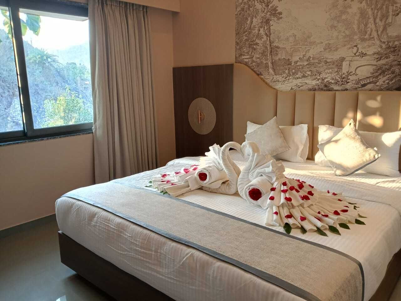 A neatly made bed with white linens and decorative swan-shaped towels with rose petals.