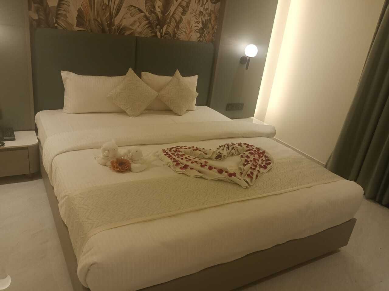 A neatly made bed with a heart-shaped pillow and a blanket, a nightstand with a lamp, and a headboard with a floral pattern.