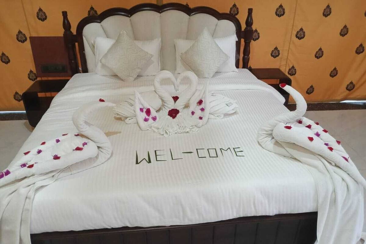 A bed with a white bedspread featuring a swan and heart design, and the words "WELCOME" on it.