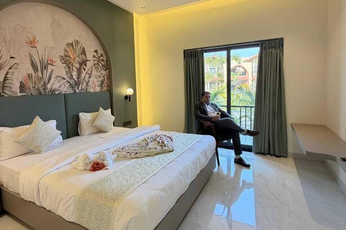 A modern hotel room with a large bed, a ceiling fan, a view of the outdoors, and a painting on the wall.