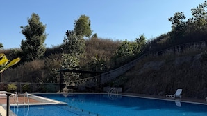 A swimming pool with a wooden deck, surrounded by a stone wall and trees.