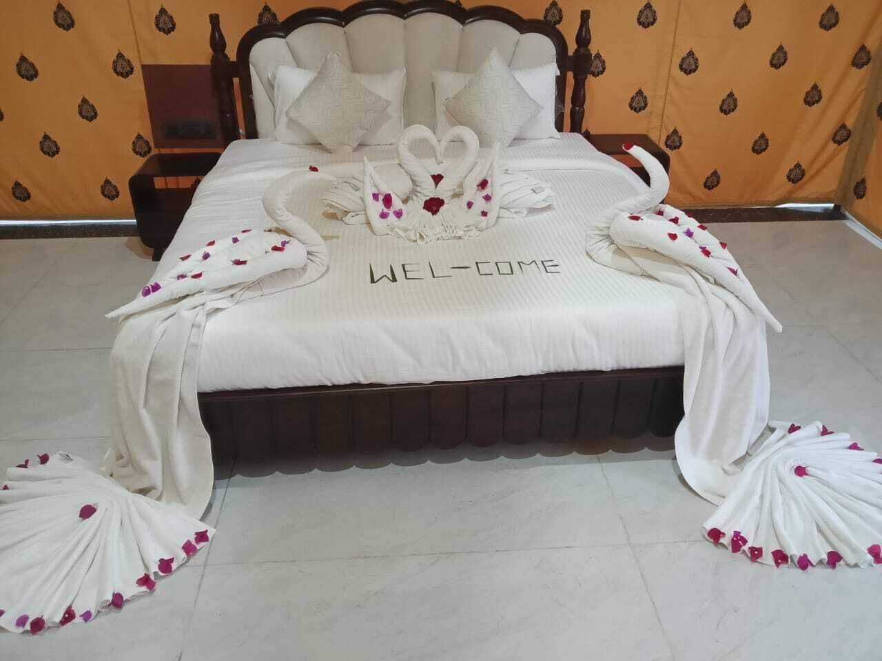 A bed with a 'WELCOME' sign, swan-shaped pillows, and a 'WEL-COME' sign on the bedspread.