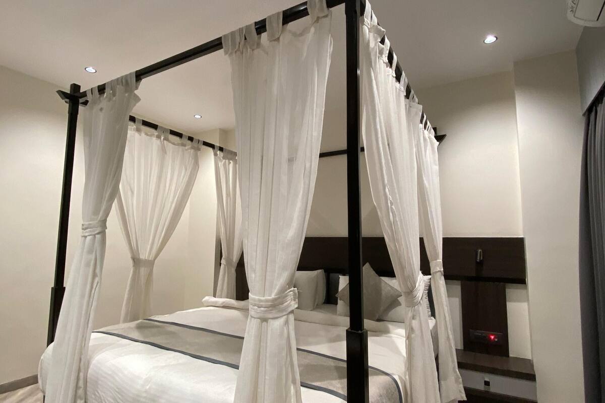 A four-poster canopy bed with white bedding and a patterned rug.