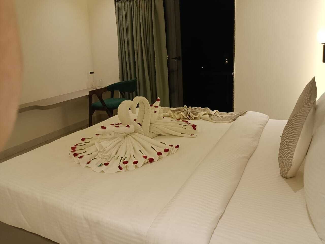 A hotel room with a neatly made bed, a chair, and a window with curtains.
