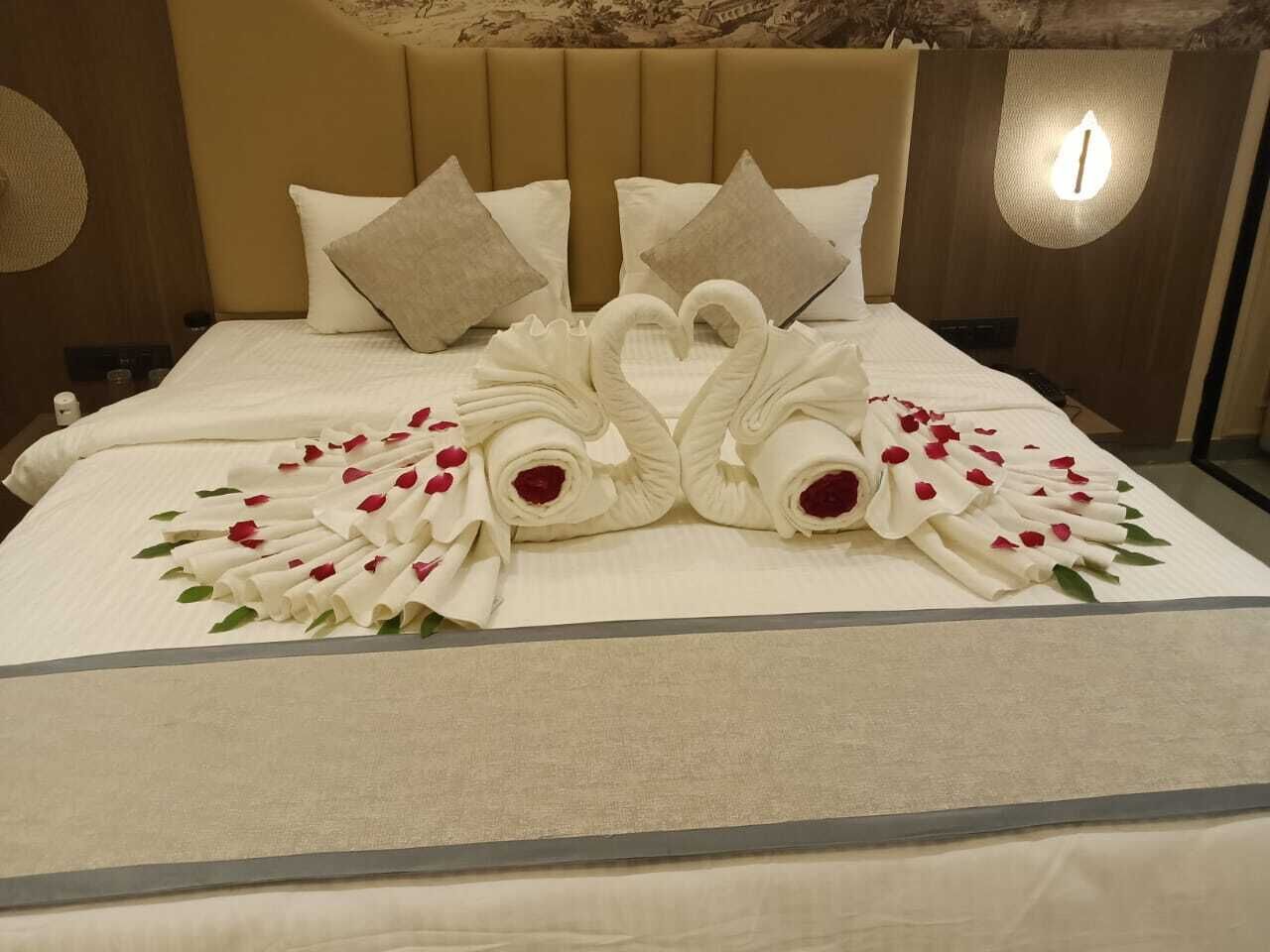 A neatly made bed with a heart-shaped towel arrangement and rose petals.