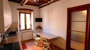 A compact kitchen with a wooden table, a window with curtains, a radiator, and a door with frosted glass panels. - Casa Carlo - Isola d`Elba (Rio Marina)