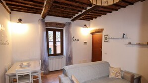 A cozy living room with a sofa, a dining table with chairs, a window with curtains, and a wooden ceiling. - Casa Carlo - Isola d`Elba (Rio Marina)