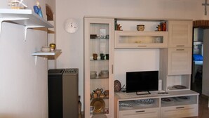 A compact living space with a built-in TV, shelves with decorative items, and a clock on the wall. - Casa Carlo - Isola d`Elba (Rio Marina)