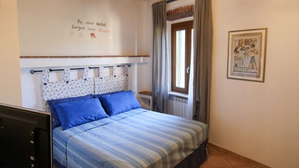 A bedroom with a bed, a headboard with a floral pattern, a window with curtains, and a wall with a framed picture. - Casa Carlo - Isola d`Elba (Rio Marina)