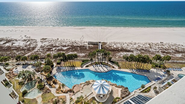 Um resort com uma piscina grande, acesso à praia e palmeiras.