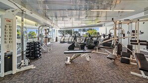 Uma academia com diversos equipamentos de exercícios, teto espelhado e amplas janelas com vista para o exterior.
