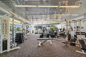 A gym with various exercise equipment, a mirrored ceiling, and large windows offering a view of the outdoors. - Remodeled 1 Bedroom 2 Bathroom W 1200 Gulf Front Condo with Stunning Views! (Pensacola)