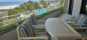 A balcony with striped chairs and a table, overlooking a beach and a pool area. - Eden E 205 Gulf Front Condo with Stunning Views! (Pensacola)