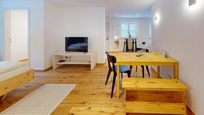 Un soggiorno moderno con pavimento in legno, una TV su un mobile bianco, un tavolo da pranzo con sedie e una scala.