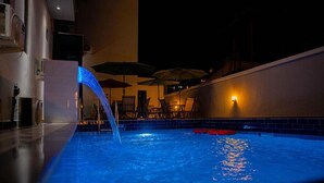 A swimming pool with a water feature, lounge chairs, and umbrellas. - Nice Royal Hotel (Abuja)