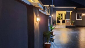 A nighttime view of a building's exterior with a paved walkway, potted plants, and outdoor seating area. - Nice Royal Hotel (Abuja)