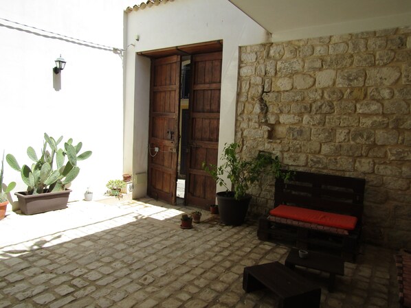 A courtyard with a wooden bench, potted plants, and a stone wall.
