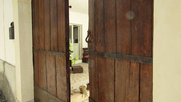 A wooden door opening to a courtyard with a bench and potted plants. - The Blue Room Courtyard (Scicli)