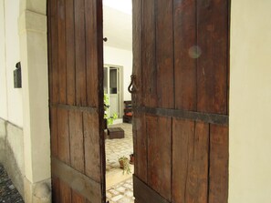 A wooden door opening to a courtyard with a bench and potted plants.