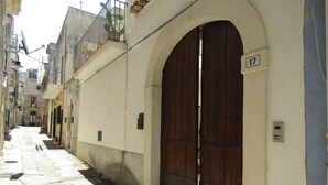 A narrow street with a large wooden door and a number 17 sign on the wall. - The Blue Room Courtyard (Scicli)