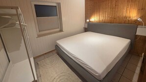 A bedroom with a bed, a window, a wardrobe, and a wooden ceiling.