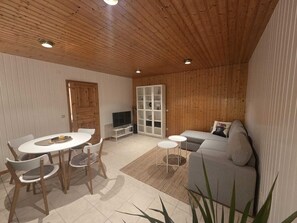 A modern interior with a wooden ceiling, a dining area with a round table and chairs, a grey sofa, and a TV stand. - LangzeitNest - Temporary living (Krummhörn)