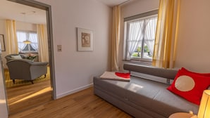 Ett modernt rum med en grå soffa, en röd kudde, en inramad tavla på väggen och ett fönster med gardiner.