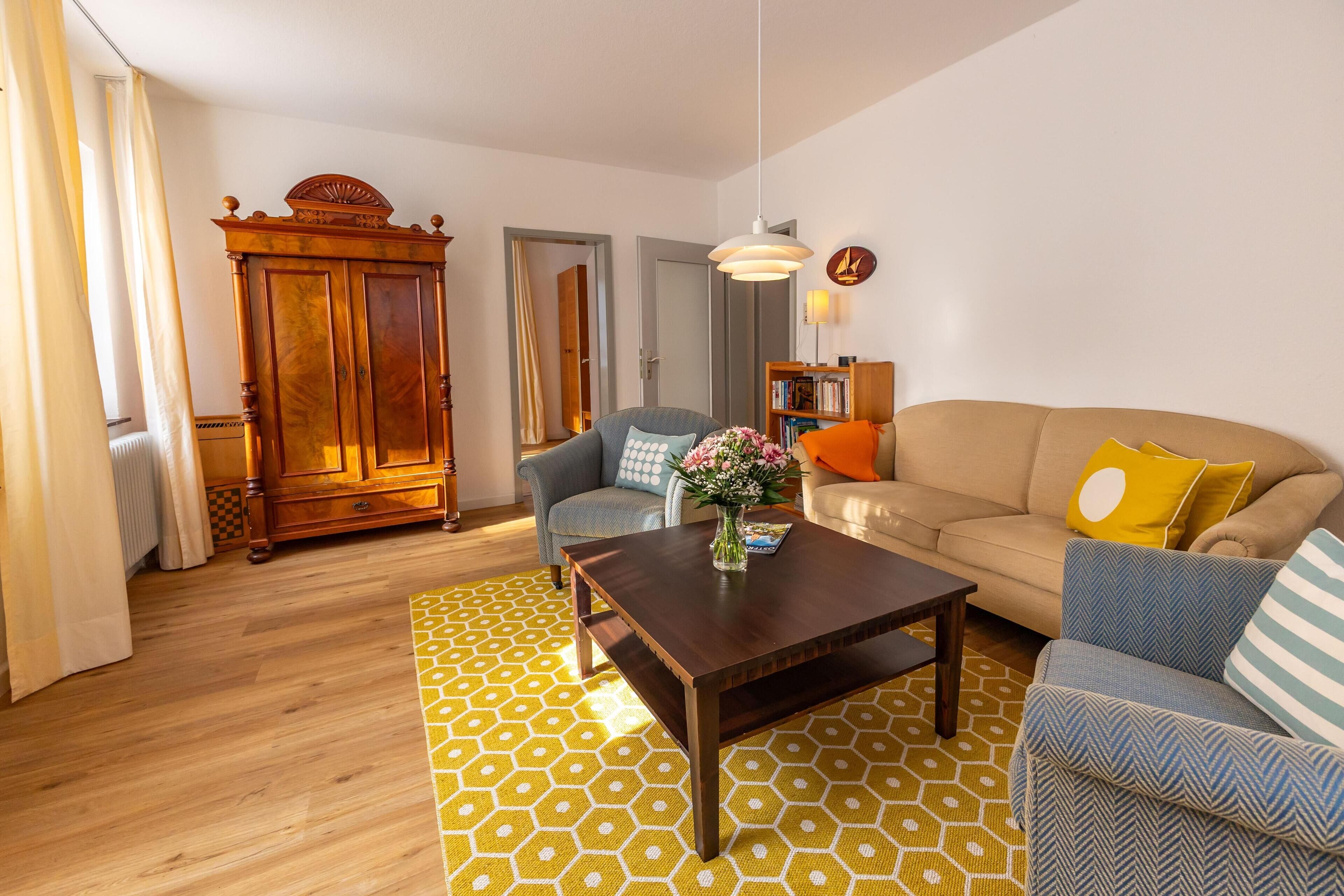Een woonkamer met een houten kast, een bank, een salontafel en een vloerkleed met dessin.