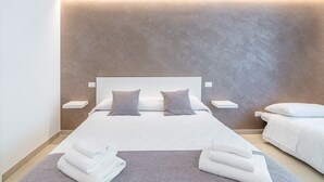 A modern bedroom with a large bed, bedside tables, and a built-in shelf. - Aura B&B - Tripla Bed and Breakfast (Pachino)