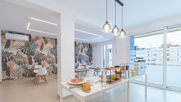 A modern interior with a dining area featuring a white table, chairs, and a buffet with food items. - Aura B&B - Tripla Bed and Breakfast (Pachino)