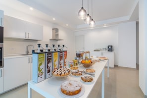 A modern kitchen with white cabinets, a central island with food items, and overhead pendant lighting. - Aura B&B - Tripla Bed and Breakfast (Pachino)