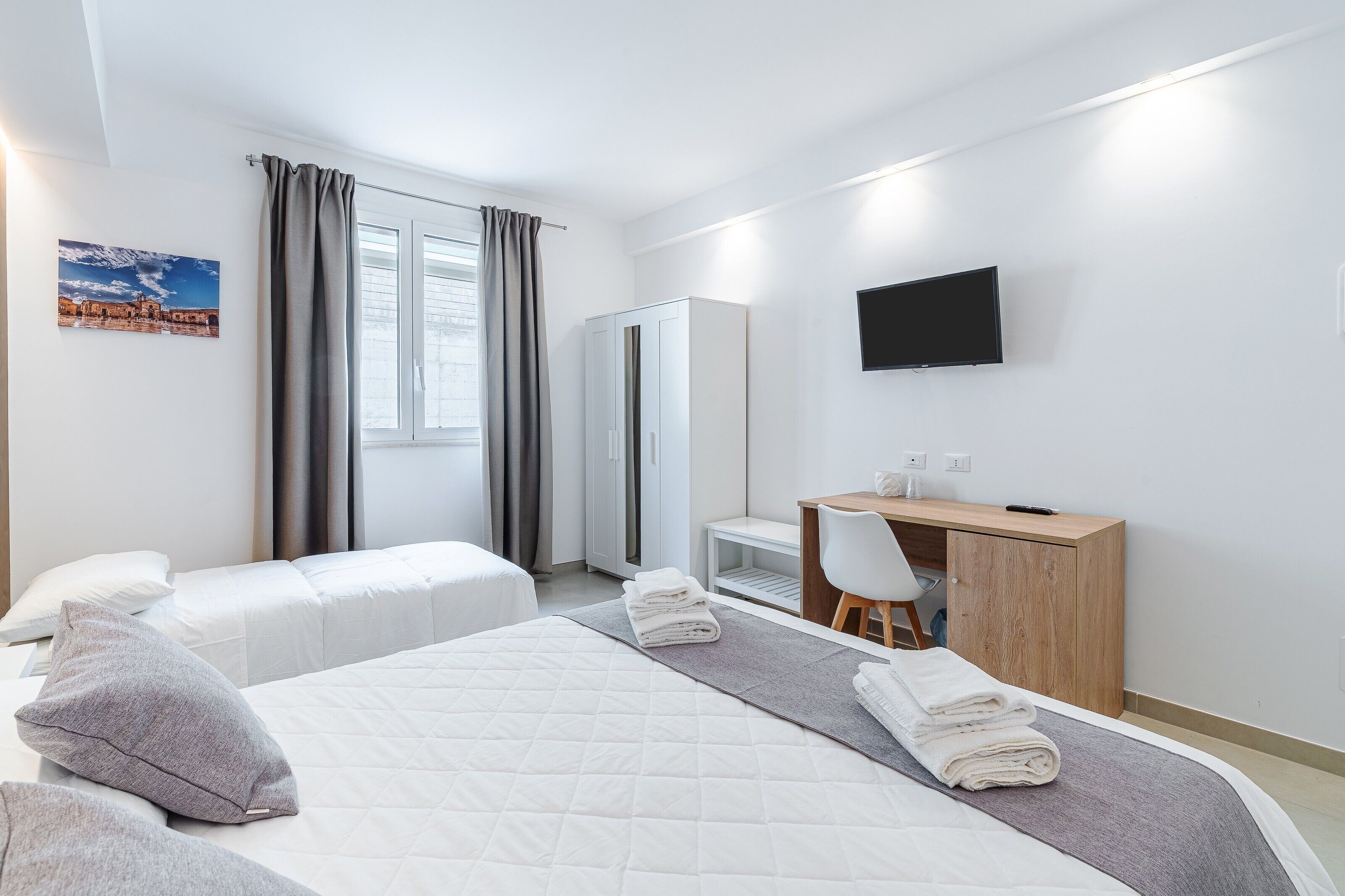 Ein Hotelzimmer mit zwei Betten, einem Schreibtisch, einem Stuhl, einem Fernseher und einem Kleiderschrank.