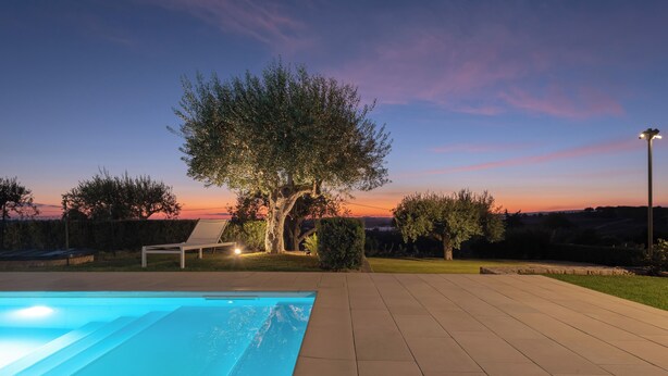 Ein Schwimmbecken mit Sonnenuntergangsblick, ein Baum und ein Stuhl.