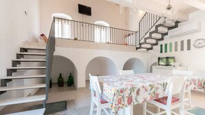 Ein Essbereich mit einem Tisch für zwei Personen, eine Treppe mit Geländer und ein Fernseher auf einem Schrank.