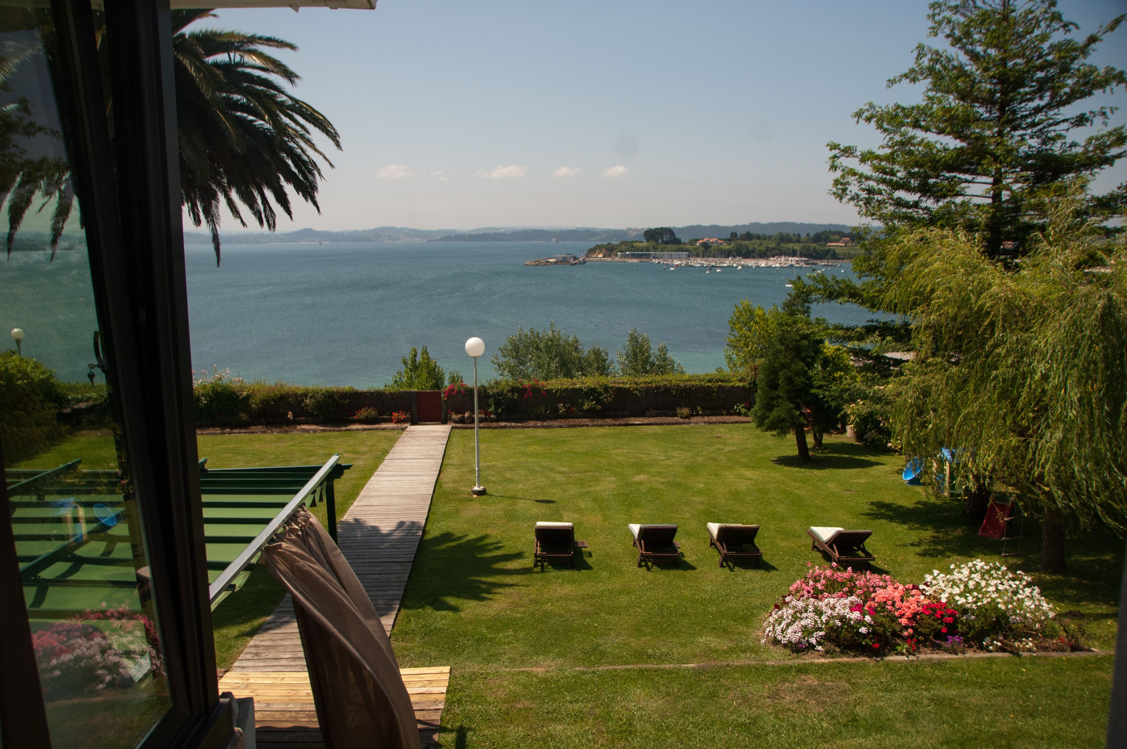 A view of a coastal landscape with a grassy lawn, outdoor seating, and a body of water in the distance.