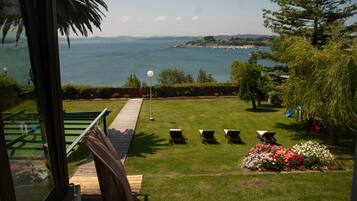A view of a coastal landscape with a grassy lawn, outdoor seating, and a body of water in the distance.
