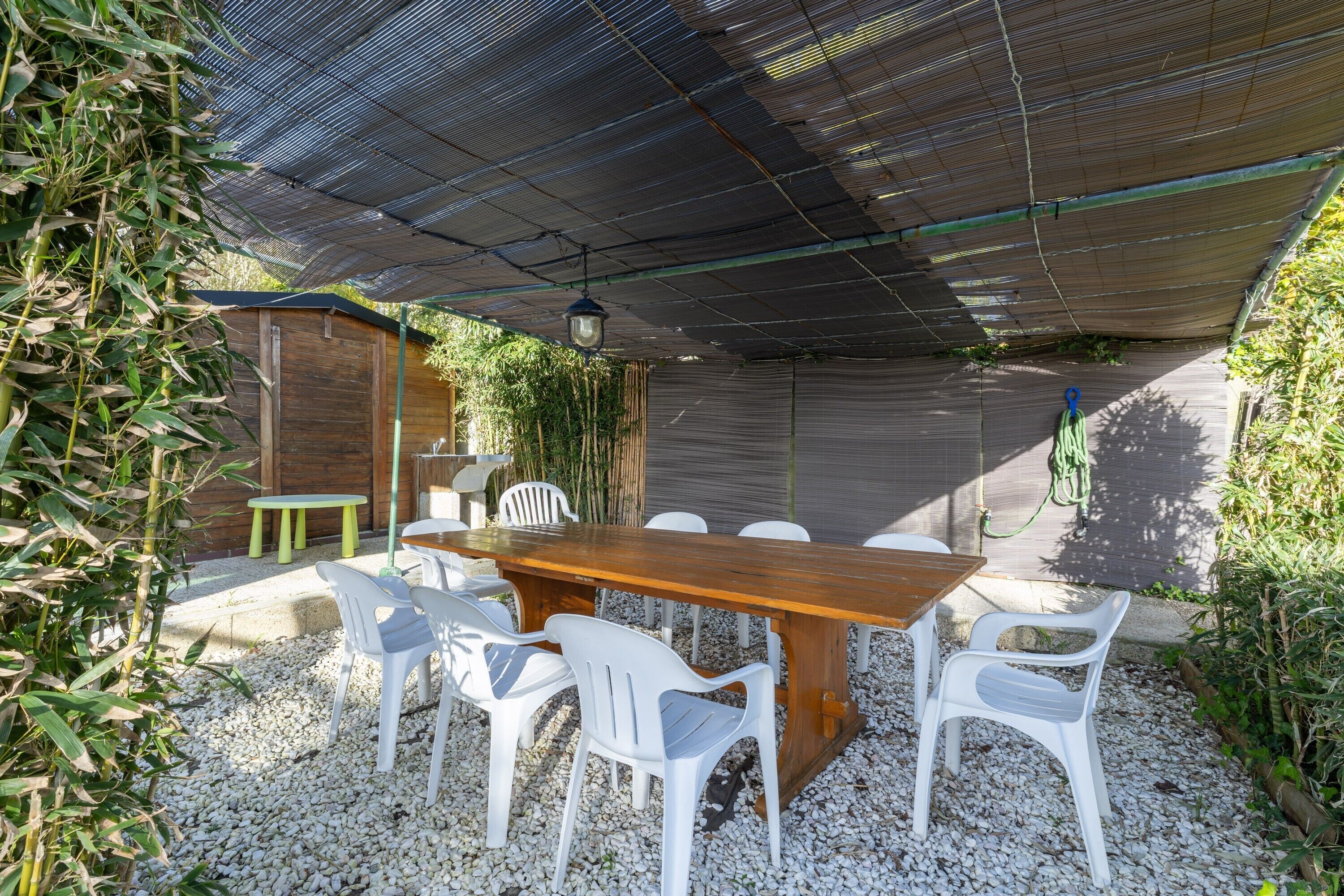 Un espacio exterior para comer con una mesa de madera y sillas de plástico blanco, rodeado de grava.