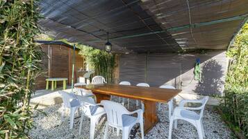 Un espacio exterior para comer con una mesa de madera y sillas de plástico blanco, rodeado de grava.