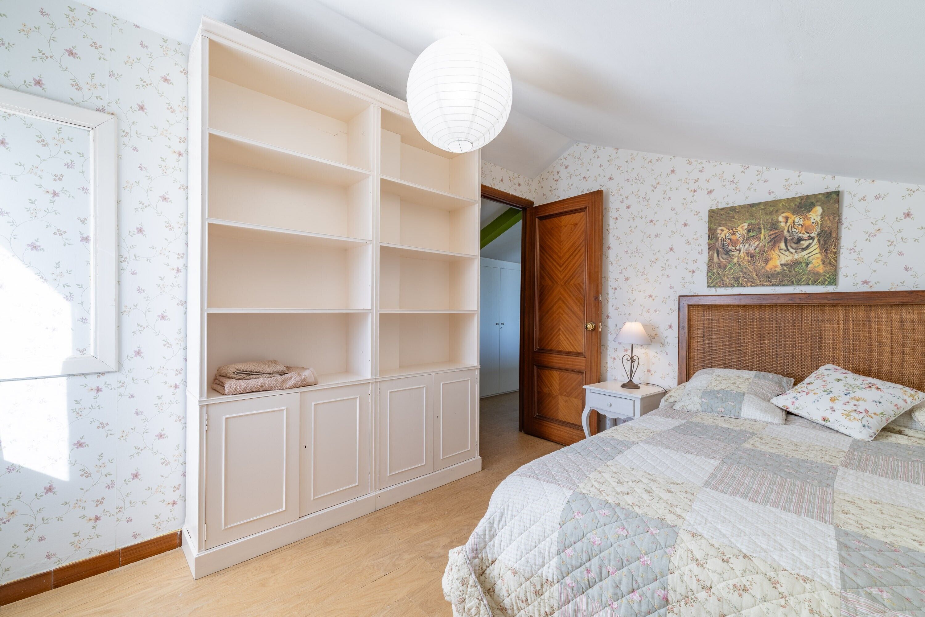 Un dormitorio con cama, armario, mesita de noche, lámpara y un cuadro en la pared.