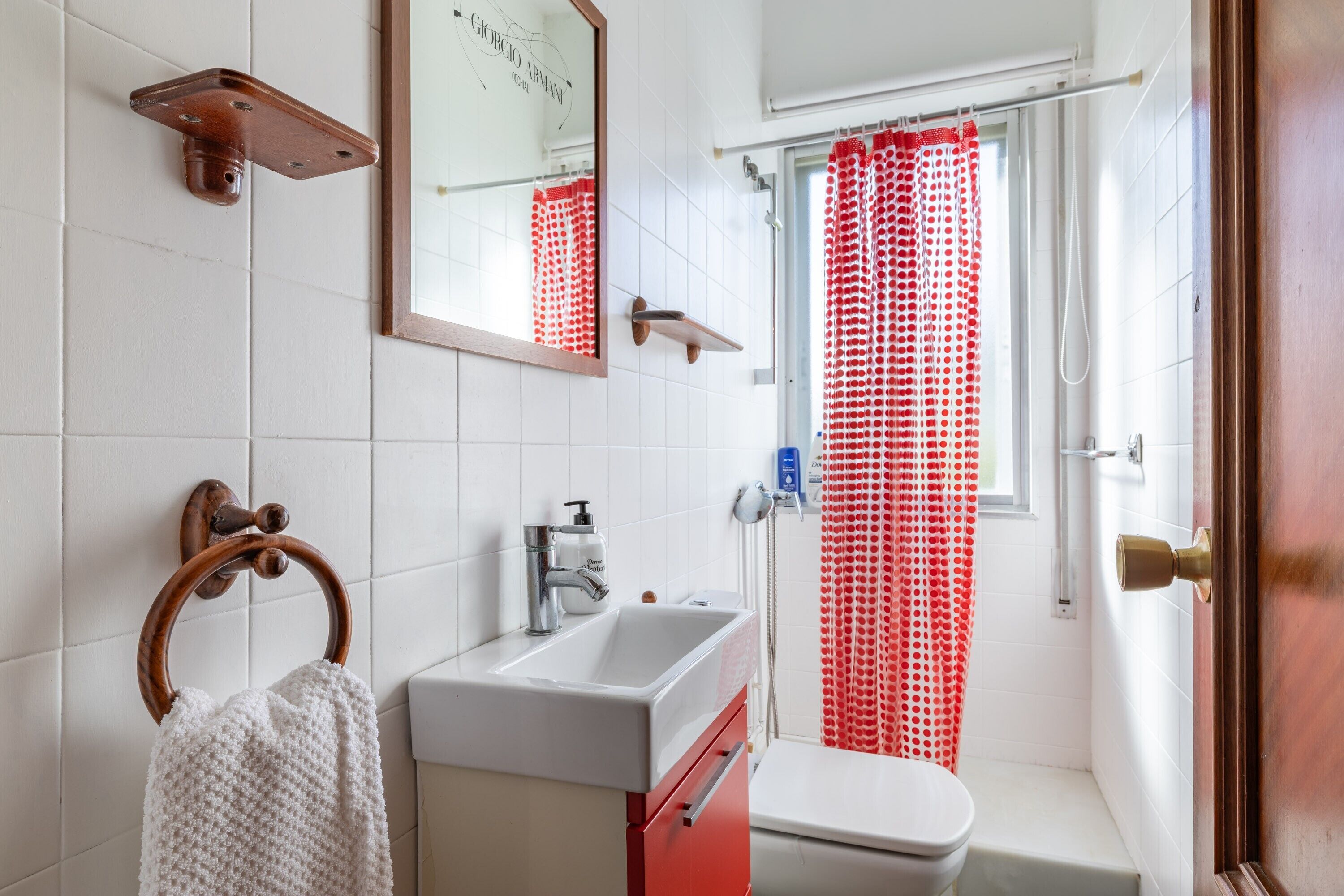 Une salle de bain avec un lavabo blanc, un miroir, un porte-serviette et un rideau de douche rouge.