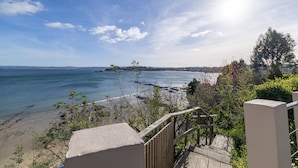 A coastal view with a wooden deck, a sandy beach, and a clear sky.