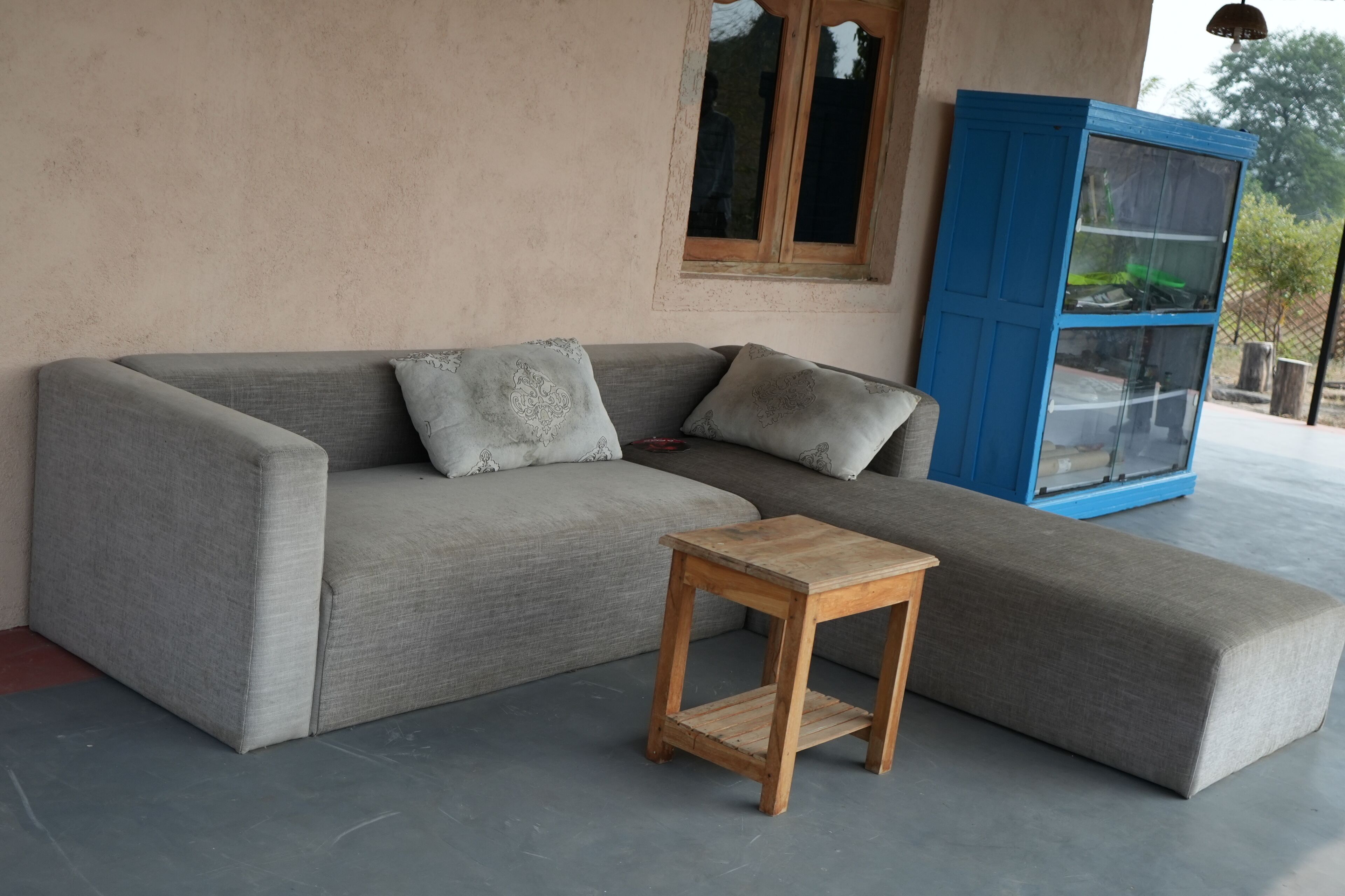 Un canap é d’angle gris avec des coussins à motifs, une petite table en bois et un meuble bleu avec des portes en verre.