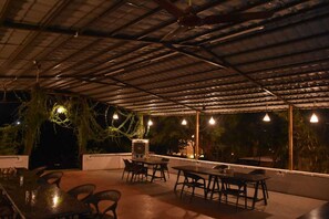 Un espace de restauration en plein air, avec des tables et des chaises, un ventilateur de plafond et des luminaires suspendus.