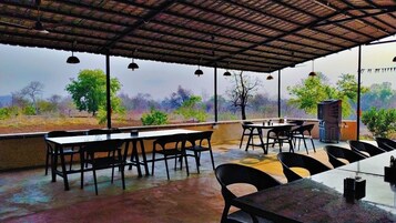 Un área de comedor al aire libre con mesas y sillas, techo cubierto y vistas del paisaje circundante.