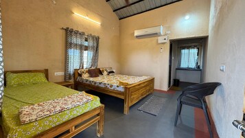 Una habitación con dos camas de madera, una mesita, una silla, un aire acondicionado y una ventana con cortinas.