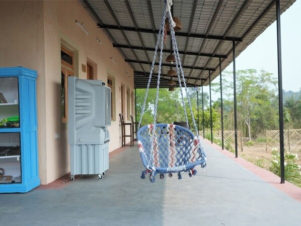 Un espace extérieur abrité comprenant un fauteuil suspendu, un meuble bleu et un réfrigérateur.